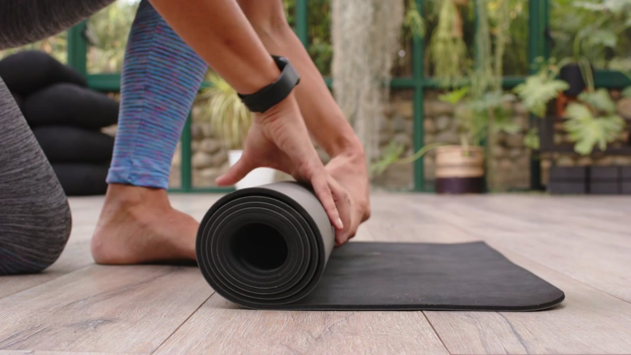 Mujer estirándose hacia adelante y tirando de una esterilla de yoga negra enrollada, desenrollándola y alisándola para la práctica de yoga.