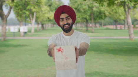 hombre indio sikh feliz dando un regalo en el parque