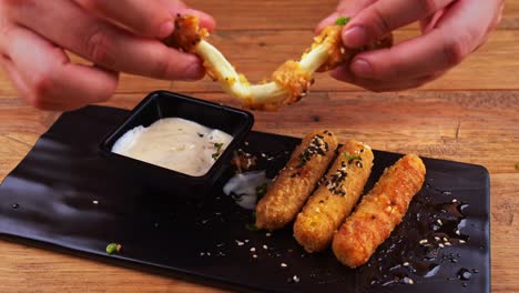 close up of a plate of cheese fingers breaded with sesame seeds, habanero peppers, ranch dressing and worcestershire sauce, cheese finger being halved and then dipped in ranch dressing