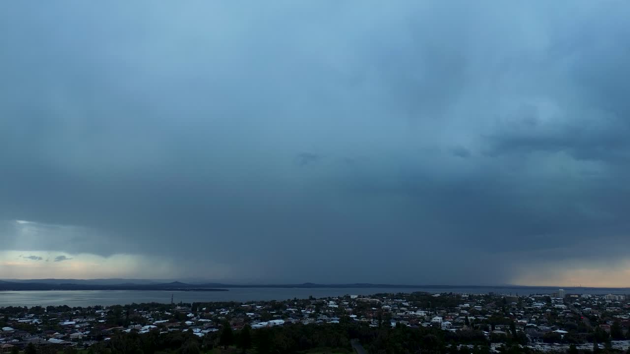 Drone aerial landscape of rural suburban town with overhead lightning strikes and rainfall from dark thunderstorm clouds in the sky at Shelly Beach Central Coast Australia weather environment nature