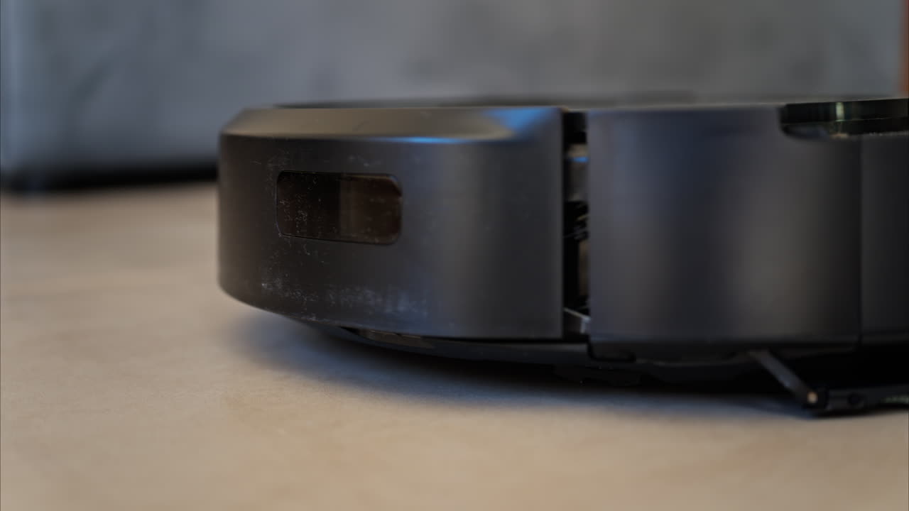 Close up of a small, black robot vacuum cleaning the house