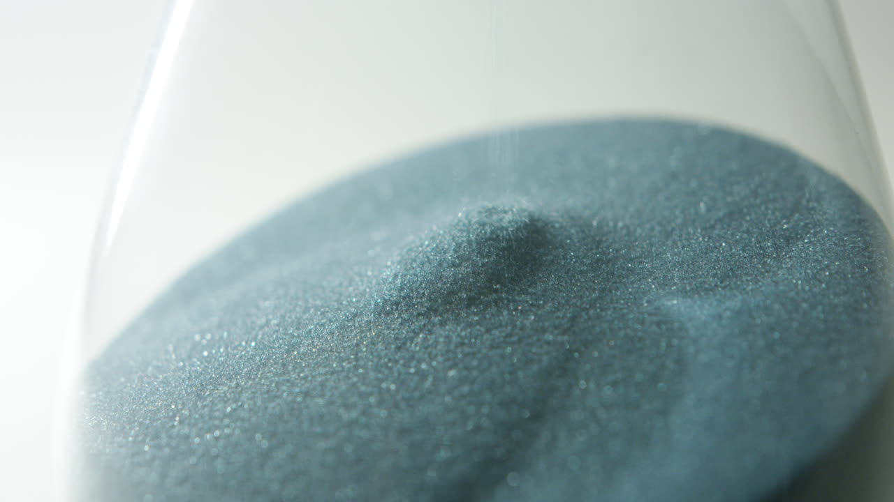 camera rotates slowly around the lower part of hour glass, showing the sand falling through in slow motion