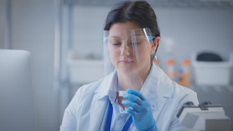 female lab worker wearing ppe face shield recording test results on computer