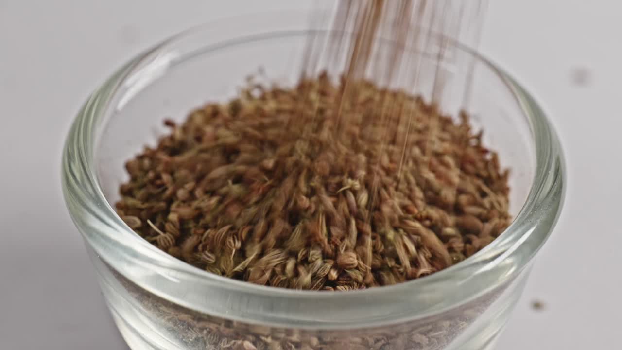 carom seeds or ajwain falling in small glass bowl, 4k, stable shot