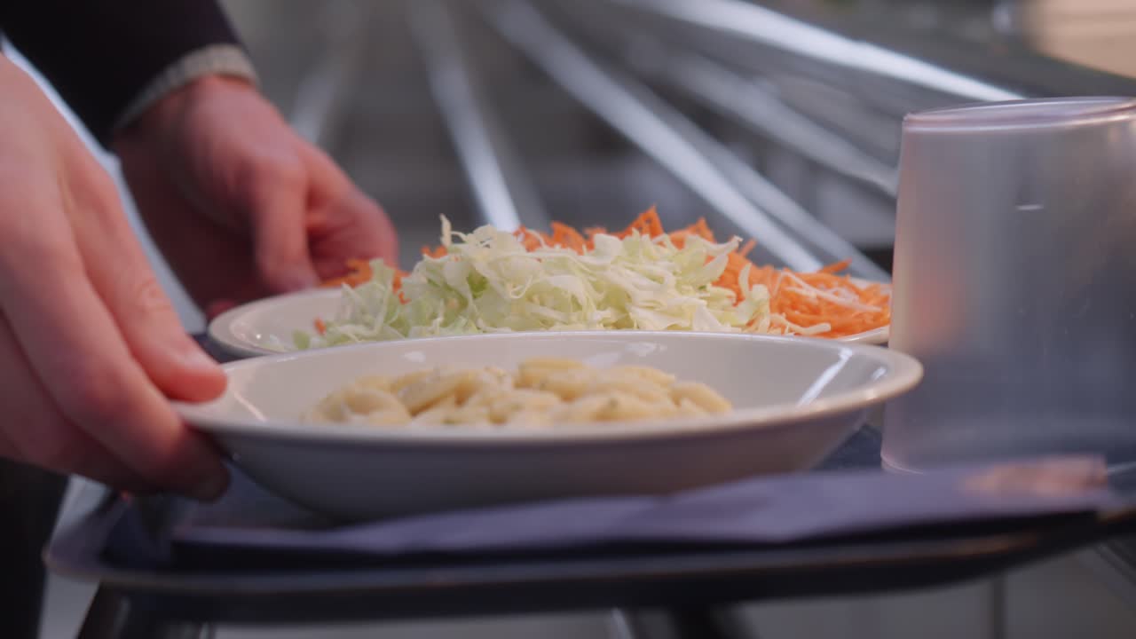 Tray with pasta and fresh salad and carrots, vegetables held by person in self-serving line.
