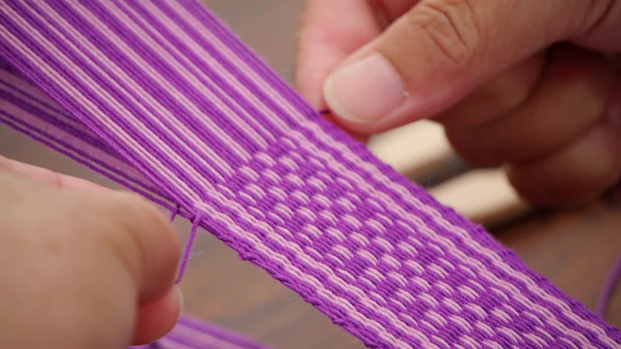 Fingers stringing and pressing purple and white yarn
