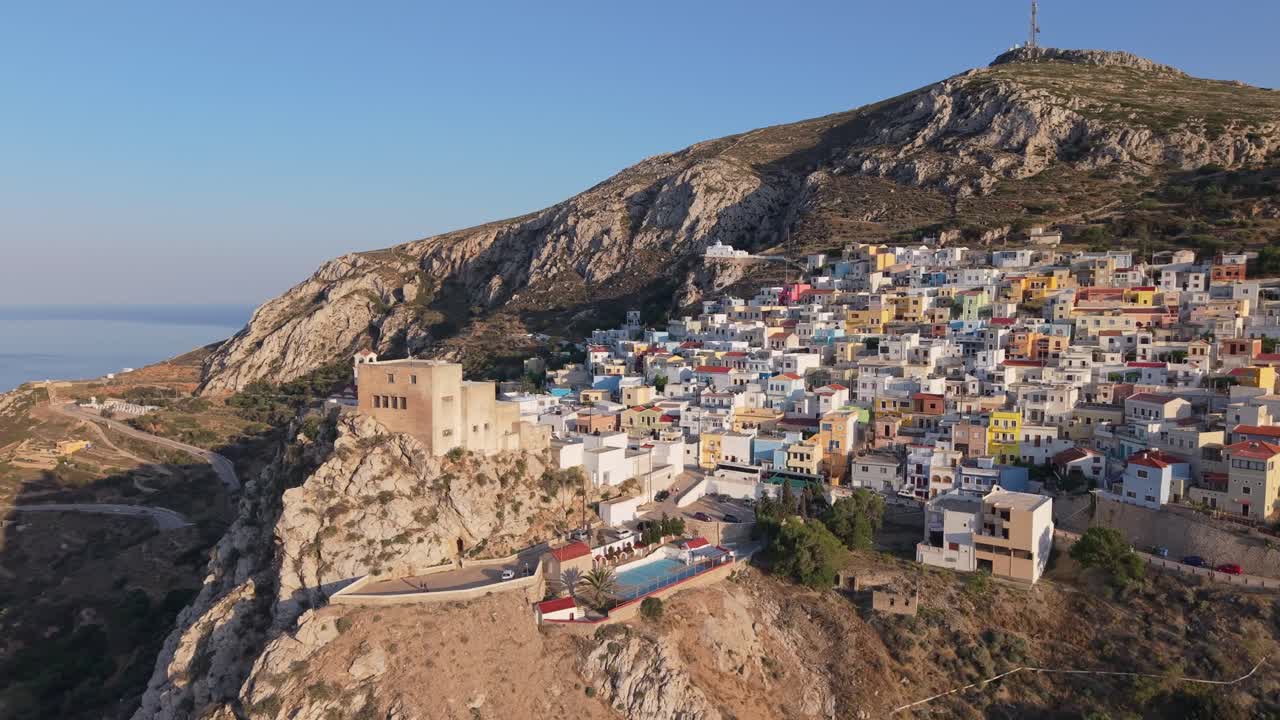 Orbiting drone footage of Menetes Village on Karpathos Island, Greece, captured in golden afternoon light revealing colorful houses and stunning Mediterranean scenery