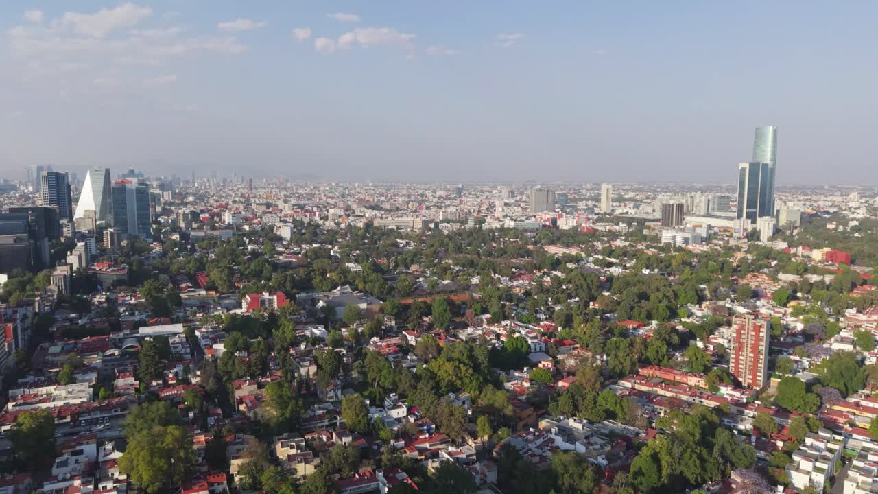 Drone view over a tree-filled area in CDMX, skyscraper in distance