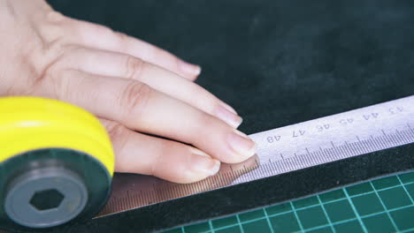 woman hand cuts black leather strip with rotary cutter