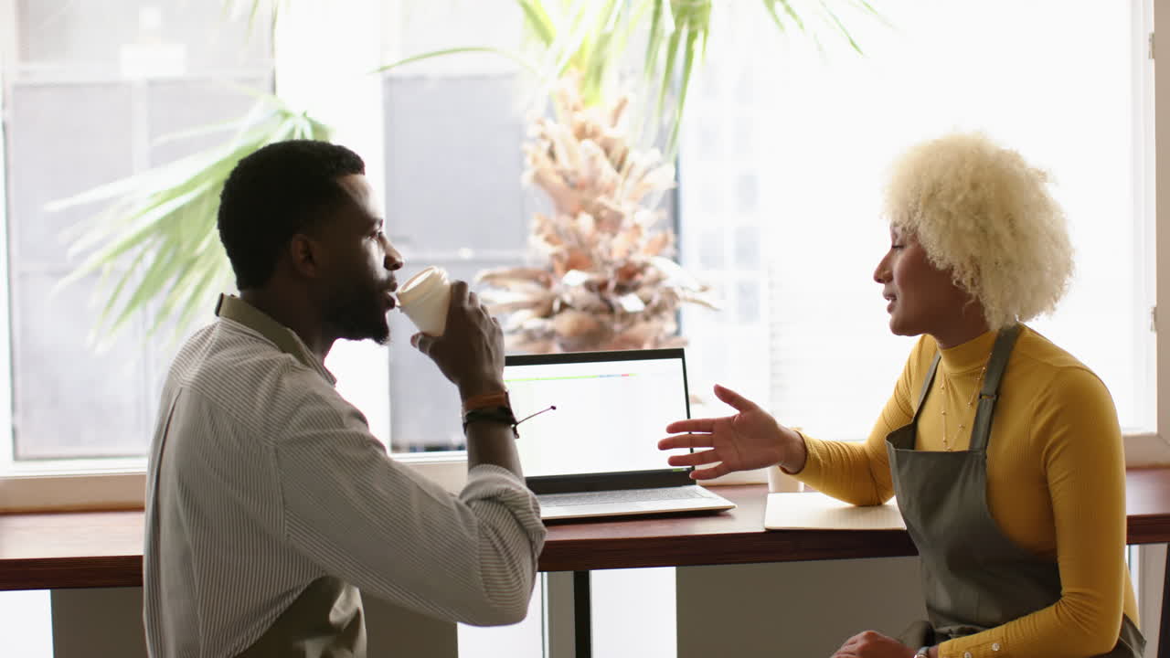 A diverse barista team colleagues discuss over a spreadsheet on a laptop