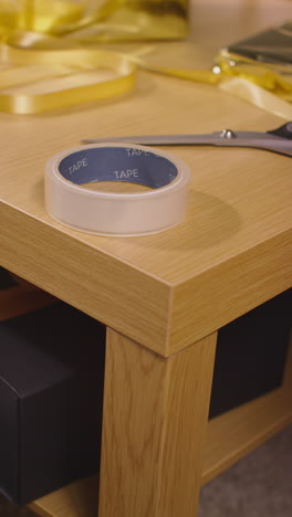 vertical video of gift or present being wrapped on table at home with scissors sticky tape and ribbon 1