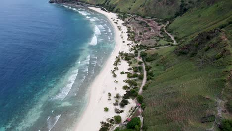 colinas verdes, mientras que la arena, el océano azul y las ondulantes olas de un destino remoto: toma aérea de drones de la playa trasera en dili, timor leste, sudeste de asia