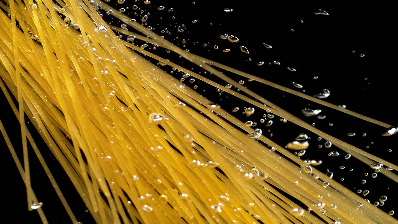 검은 바탕에 물에 떨어지는 파스타 줄기 - 거시 및 느린 동작으로 스파게티를 조리