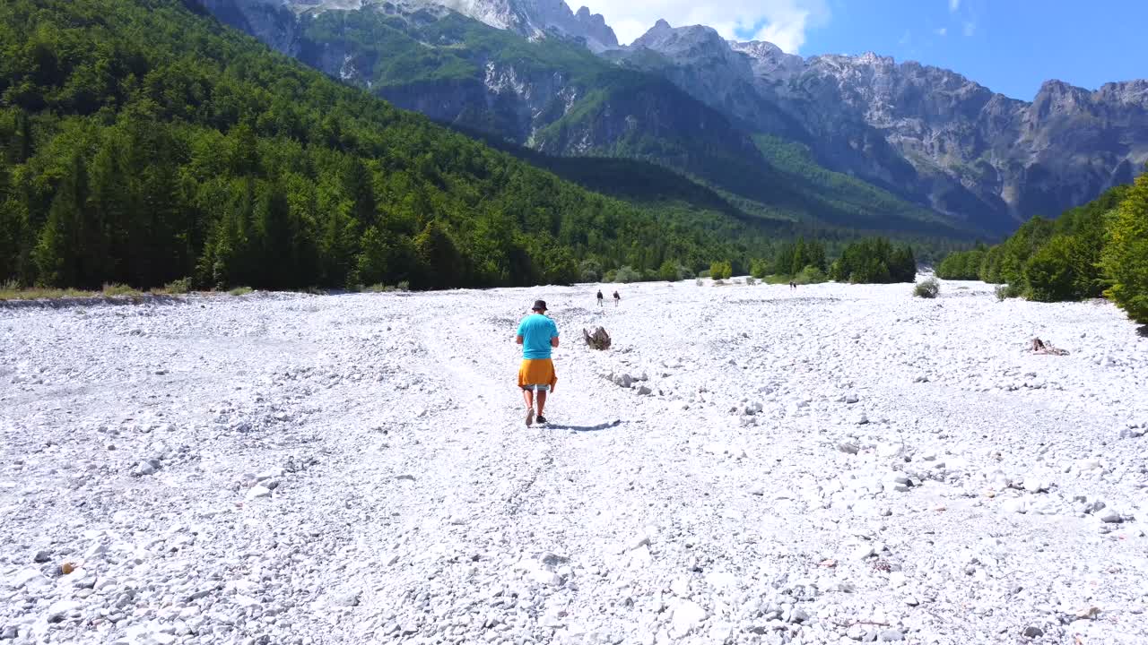 People Walking in a Rocky Riverbed with Mountains