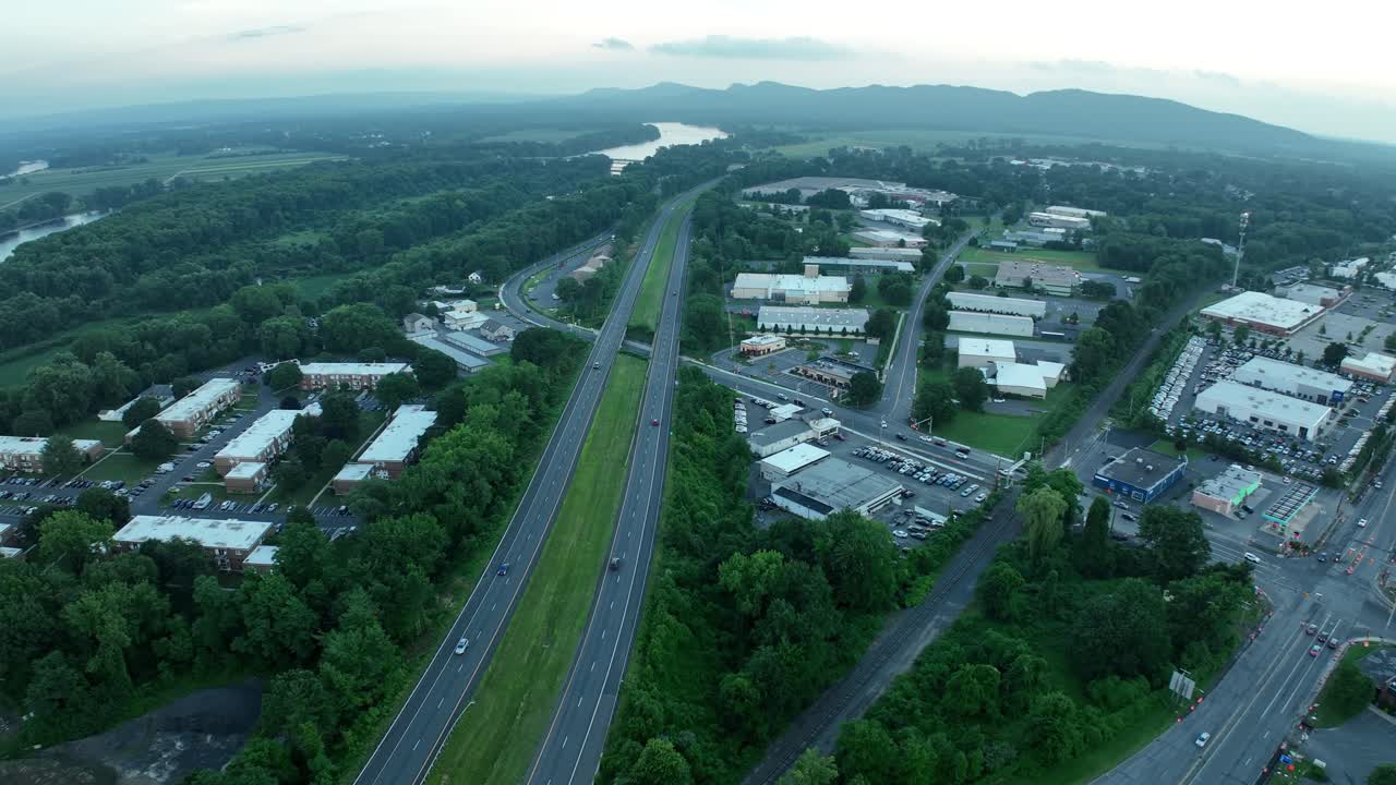 Panoramica aerea di un'autostrada che si estende verso le montagne in lontananza, con un'area verde lussureggiante ai lati della strada