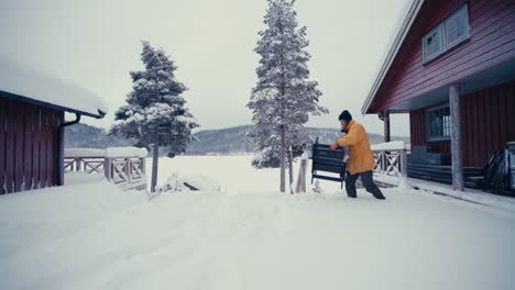 european man places wooden chair in deep snow outside the cabin during winter