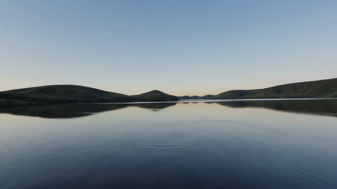 Tranquil Lake Reflecting Green Hills Under a Clear Sky