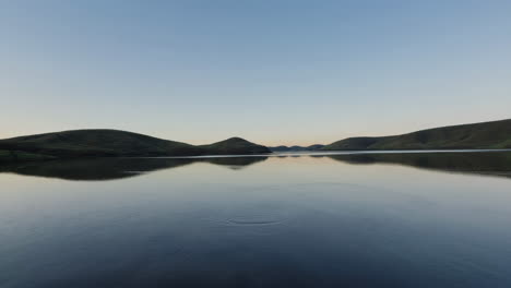 tranquil lake reflecting green hills under a clear sky