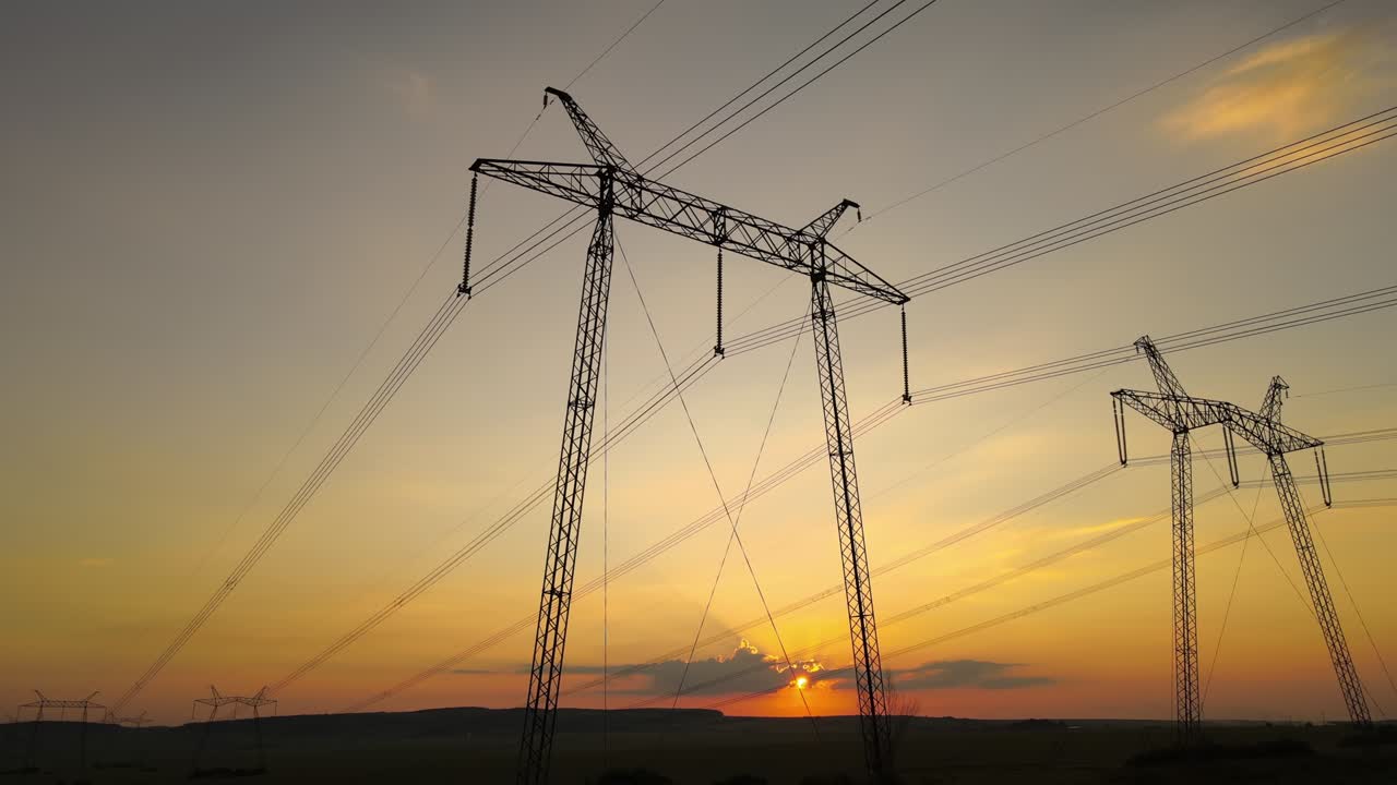 Dark silhouette of high voltage towers with electric power lines at sunrise