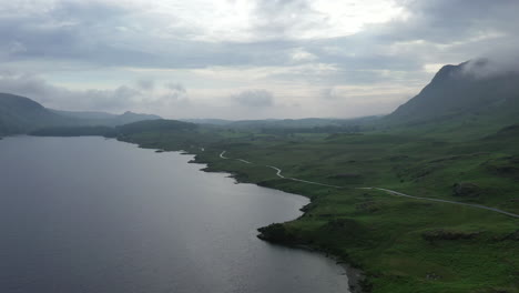 Aerial-shot-of-a-rural-road-next-to-a-lake-in-the-English-lake-district,-on-a-cloudy-day