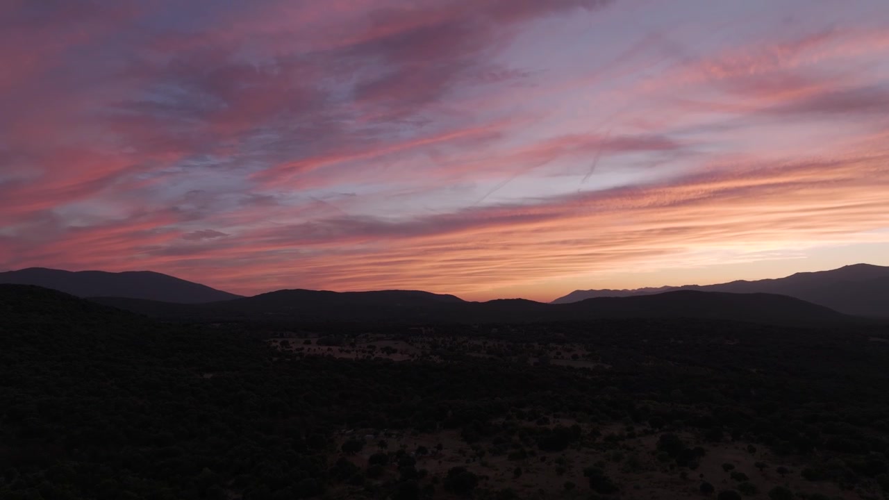 An ascending drone flight over the Tiétar Valley at sunset, revealing dark rural landscapes beneath the Sierra de Gredos and a spectacular sky filled with vibrant hues.