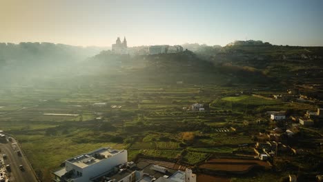 disparo de un dron alejándose de la iglesia de mellieha en una colina en una mañana muy nublada en malta