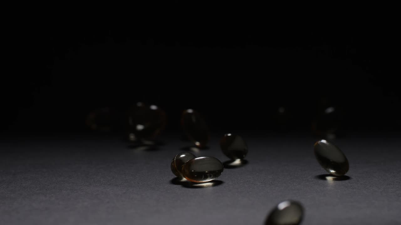Omega fish oil pills dietary supplement falling down on black background. Omega fish oil softgels dietary supplement background. Healthy life and heart health concept.