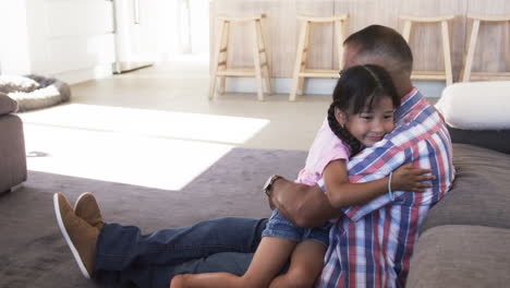 abuelo biracial abrazando a su nieta en el sofá, ambos sonriendo