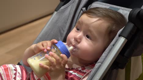 pretty baby girl drinks milk from bottle lying in a stroller, face close-up