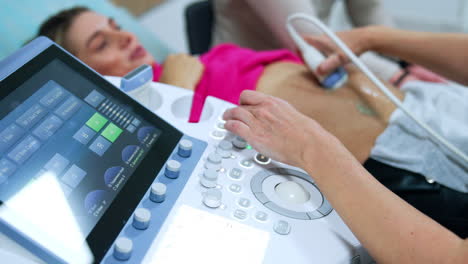 ultrasound machine is used to check up the pregnancy development. doctor moves the device by the belly of blonde woman.