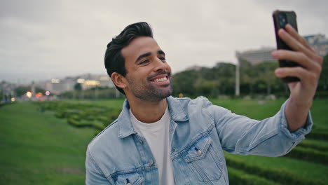 saludando a un turista sonriente con una cámara web de teléfono inteligente relajándose en un parque verde de cerca