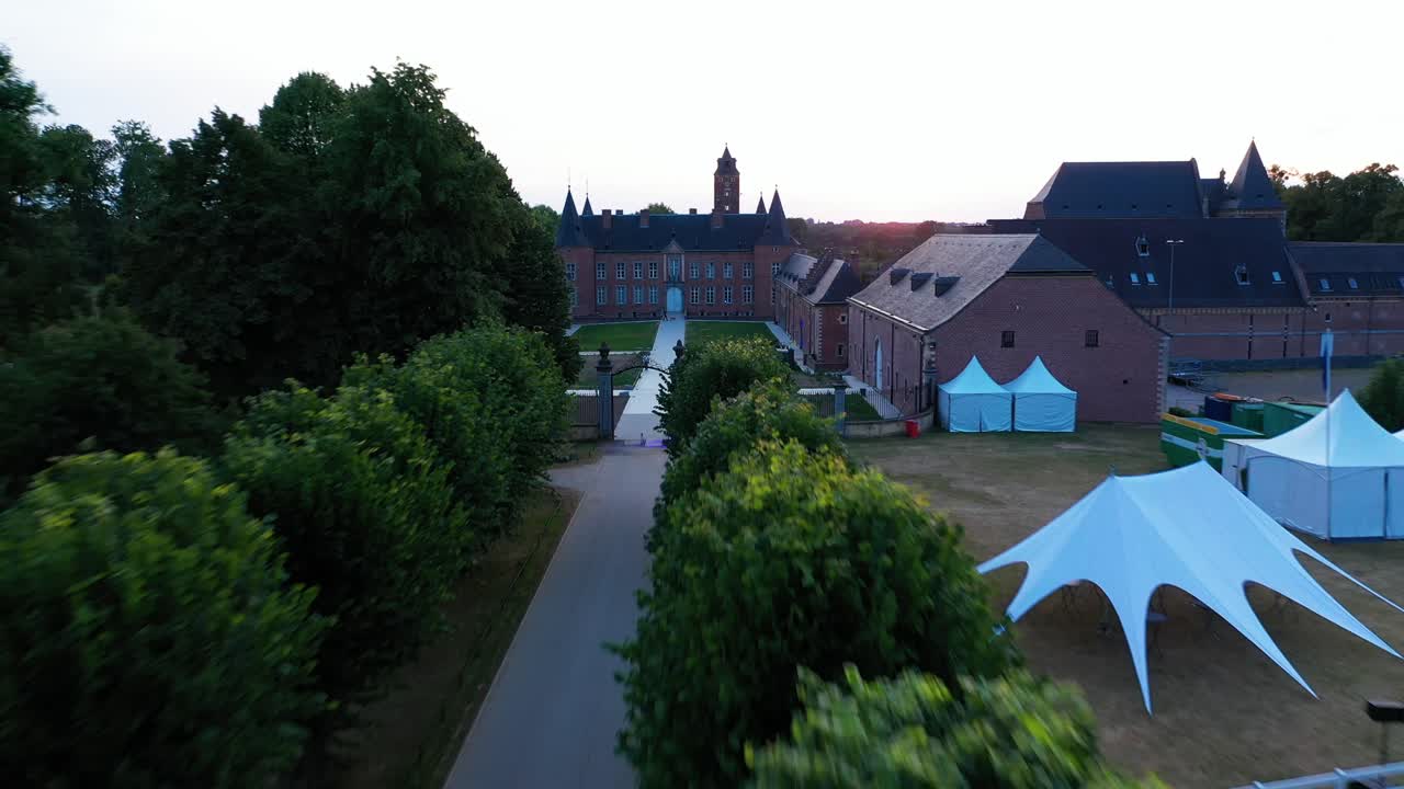 벨기에에 있는 알덴 비센 성의 입구와 정원의 공중 전망, 독일은 입구 통로에서 개와 함께 걷는 사람들과 함께 낮 동안 녹지와 풍경이 있는 넓은 지역에 퍼져 있습니다.