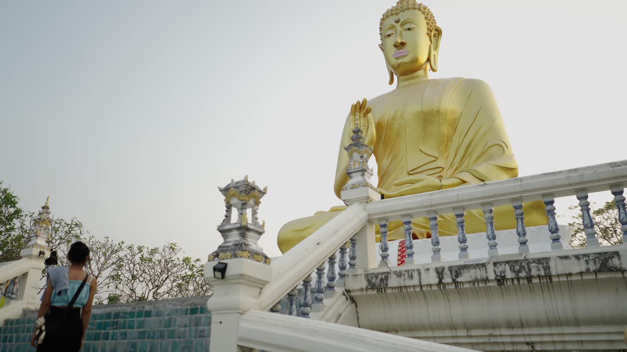 Woman approaches a large golden Buddha statue at a temple