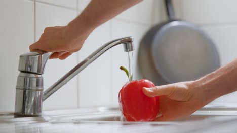 man rinsing a bell pepper under the kitchen faucet