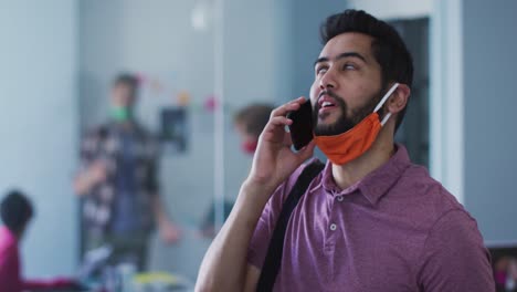 Mixed-race-man-with-face-mask-talking-on-smartphone-in-office