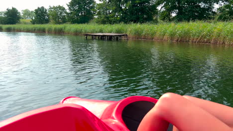 adult woman sailing a red water bike on the lake, an old wooden pier by the shore