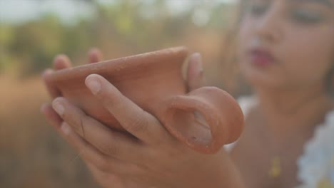una joven y hermosa mujer india inspecciona con ternura una olla tradicional de arcilla roja en sus manos
