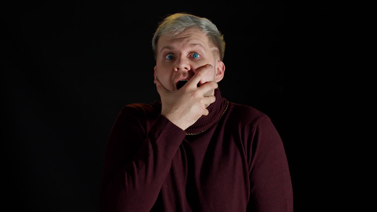 충격에 빠진 세련된 남자는 흥분을 느끼고 카메라를 보고 얼굴 근처에 손을 들고 놀랐다.