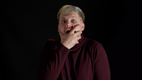 sorprendido hombre elegante sintiendo emoción, mirando a la cámara y sosteniendo las manos cerca de la cara