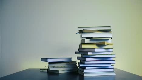 stop motion footage of books piling up on top of each other frame by frame in timelapse mode on a table. books are hardcover with white, yellow pages. pile increases and then decreases on the table.