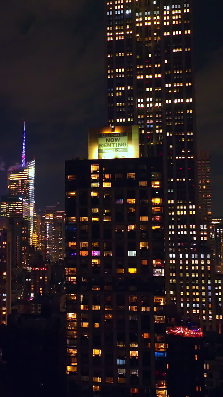 Fantastic skyscrapers with lights in windows. Wonderful buildings at the backdrop of night cloudy sky. Vertical video
