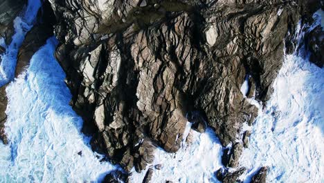 Olas-Blancas-Del-Océano-Rompiendo-Sobre-Rocas-Programadas-En-Cornwall-En-Cámara-Lenta-Con-Una-Vista-De-Arriba-Hacia-Abajo-Desde-Un-Dron-Aéreo