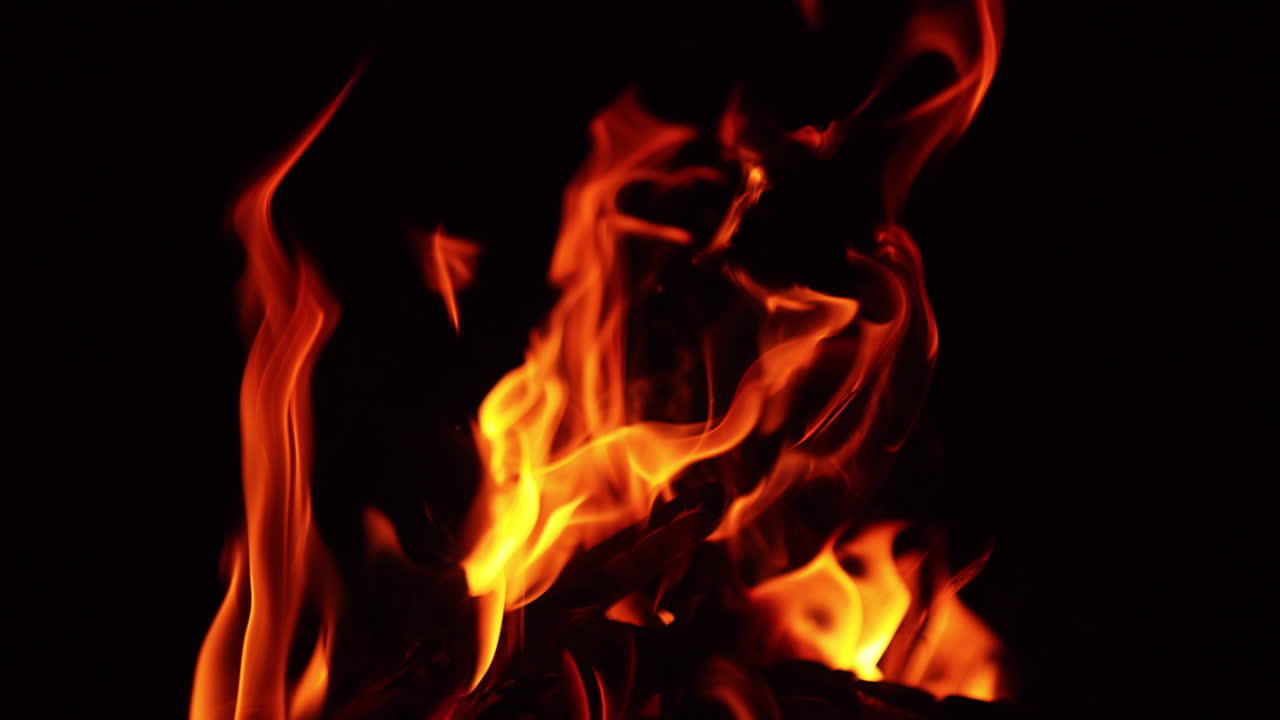 Chops of wood burn in the bonfire. Hot sparks rise up into the darkness. Close up.