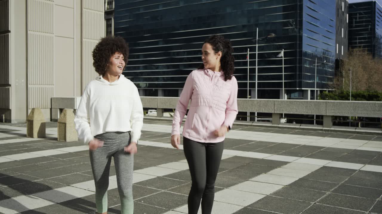 Duas mulheres em um telhado com smartwatches realizando alongamentos e afundos, e depois correndo para aquecer.
