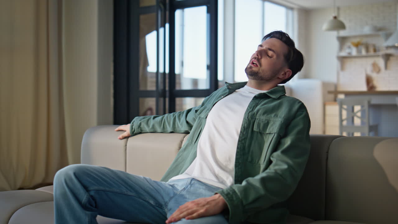 Closeup man falling sofa feeling tired at home. Weary guy taking rest sitting