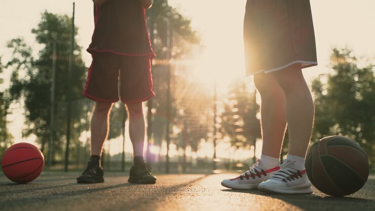 Close-up de Dois Jogadores de Basquete Alongando os Tornozelos, em uma Quadra de Basquete ao Ar Livre