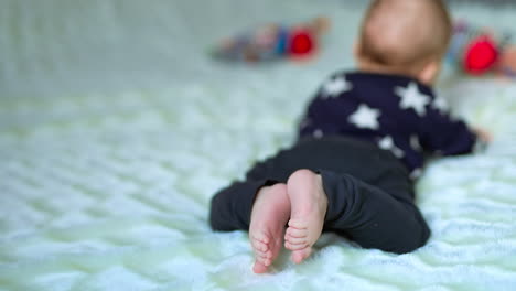 tiny toddler boy lying on belly and moving little bare feet. close up. bright toys in front of baby in blur at backdrop.