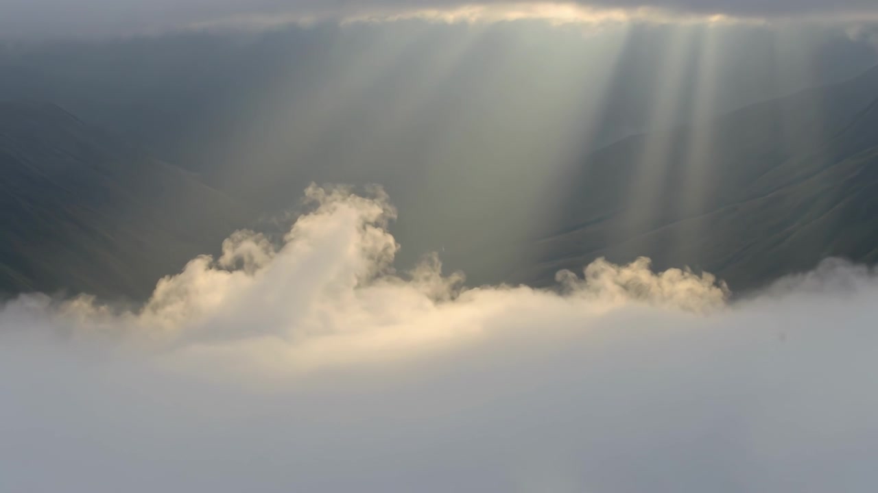 Apertura di varchi nuvolosi che lasciano passare raggi di sole che illuminano il manto nuvoloso da una vista dalla cresta, con un ciuffo di cumuli in crescita