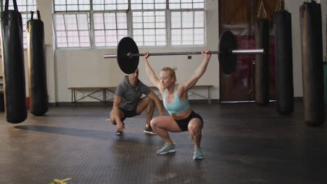 mujer caucásica en forma trabajando con barra con entrenador masculino en el gimnasio