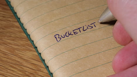 Closeup-of-hand-writing-bucket-list-into-blank-notebook